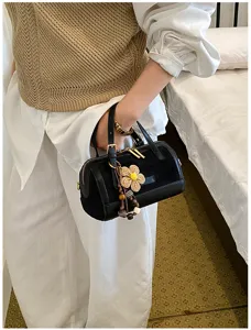 Detailed view of a stylish black cylinder pillow bag featuring a chic woven flower charm.