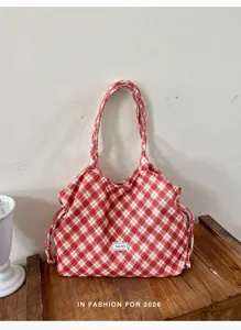 Dettaglio della borsa a spalla in tela con motivo a quadri rossi, pratico stile casual.