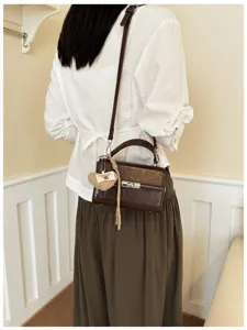 Close-up detail of a dark brown retro crossbody bag featuring a woven heart tag and clasp.