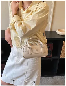Gros plan d'un sac à bandoulière minimaliste crème avec poignées et texte en relief.