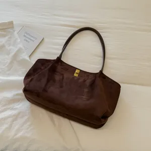 Close-up detail of dark brown suede shoulder tote bag with gold lock and slim straps.