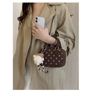 Detail shot of brown polka dot bowling shoulder bag with cute plush doll charm for women.