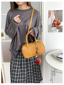 Detailansicht einer stilvollen gelben geflochtenen Boston Handtasche mit Quastenanhänger.