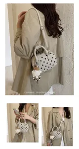 Detail view of a chic polka dot bowling handbag with cute plush pendant and adjustable strap.