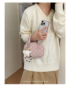 Detailed shot of trendy polka dot bowling handbag with cute furry keychain in stylish setting.