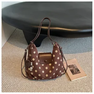 Detailopname van bruine polkadot schoudertas met lederen flap en hangende bedel erbij.