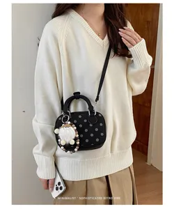 Detailed shot of black polka dot bowling bag with furry pendant, worn on model, chic retro style.