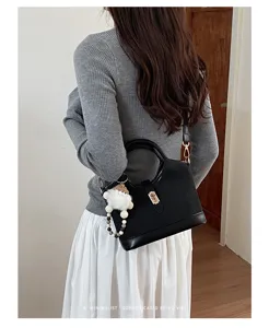 Stylish black top handle shoulder bag detail shot, featuring metal buckle and cute plush charm.
