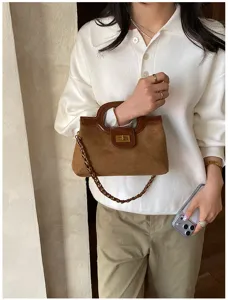 Primo piano di una borsa in camoscio marrone con manico rotondo e catena elegante.