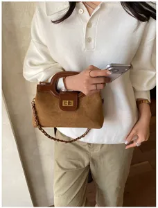 Vista dettagliata di una borsa in pelle marrone con chiusura e tracolla a catena.