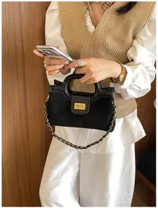 Dettaglio di borsa in pelle scamosciata nera con chiusura metallica e catena chic.