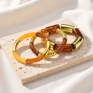 Detalle de los brazaletes elásticos curvos de resina retorcida y metal dorado estilo Maillard.