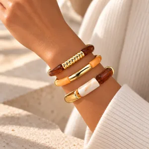 Vista detallada de pulseras superpuestas de resina y tubo de metal dorado, joyería elegante.