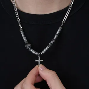Gros plan du collier croix, avec des ressorts métalliques élégants et des perles sombres.