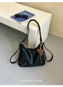 Detailed view of black multi-way shoulder bag with knit heart charm and zipper pockets.