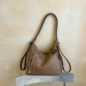 Brown convertible shoulder backpack detail featuring a cute knitted heart charm and front pocket.
