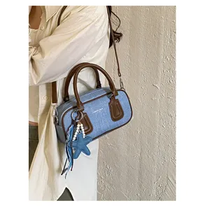 Close-up detail of stylish denim Boston shoulder bag with brown leather trim and cute starfish pendant.