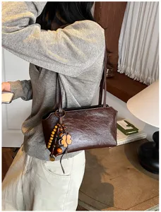 Nahaufnahme Detail einer braunen Leder Achseltasche mit hölzernem Kleeblatt Anhänger.