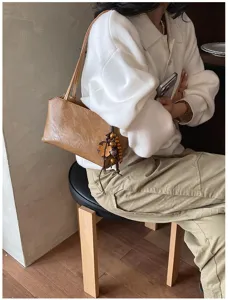 Detailansicht einer schicken braunen Leder-Achseltasche mit Perlenanhänger im gemütlichen Innenraum.
