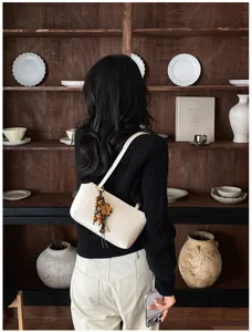 Detail der minimalistischen Schultertasche aus Creme-Leder mit stilvollem Holzperlen-Anhänger.