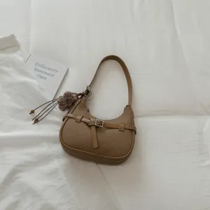 Vista de detalle de bolso de hombro marrón con correa de hebilla de metal y colgante de flor.