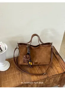 Braune Wildleder-Handtasche mit Schultergurt und kariertem Mützen-Anhänger für Damen.