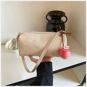 Gedetailleerd overzicht van een beige geweven cilindrische schoudertas met schattige appelhanger.