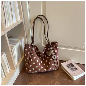 Détail de sac cabas marron à pois, présentant une matière douce et un charmant pendentif.