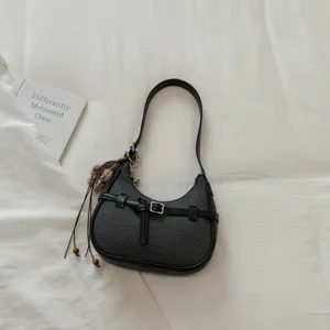 Vista detallada del bolso de hombro negro tejido en diseño crescent con cinturón y borla.