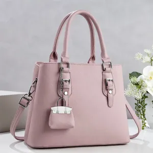 Bolso de mano de cuero rosa para mujer con asa, correas decorativas y mini colgante de bolsa.