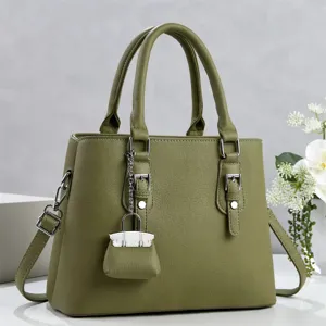 Primer plano del bolso de mano de cuero verde oliva con diseño estructurado y dije en miniatura.