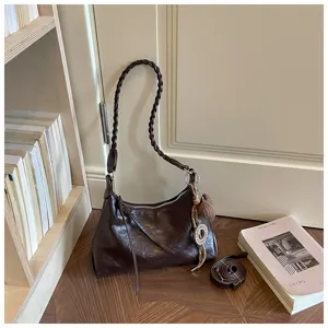 Détail de sac à bandoulière vintage marron, avec sangle tressée et charm décoratif.