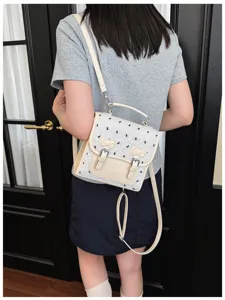 Detail view of mini white backpack with cute black bow embroidery, adjustable leather straps.