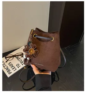 Brown suede bucket bag detail featuring a cute four-leaf clover charm and drawstring.