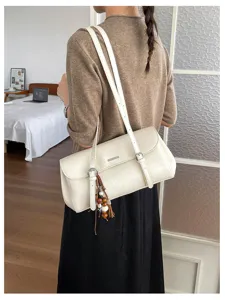 Detailed view of a retro white shoulder underarm bag with chic tassel pendant and metal hardware.