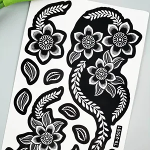 Black white floral tattoo sticker detail, intricate leaf design body art sheet close up.