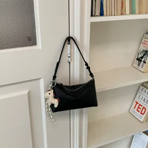 Λεπτομερής εικόνα μινιμαλιστικής μαύρης τσάντας ώμου με χαριτωμένο μενταγιόν.