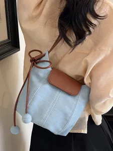 Κομψή γυναικεία τσάντα bucket denim με καφέ δερμάτινο καπάκι και μπάλες κορδονιού για καθημερινή χρήση.