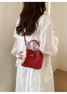 Detail view of a chic red bucket bag with turn-lock closure and cute plush bear charm.