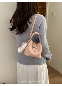 Minimalist pink leather bucket bag with metal lock clasp and cute plush pendant accessory.