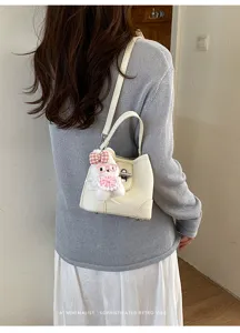 Stylish white bucket bag detail shot showcasing shoulder wear and cute rabbit pendant.