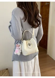Minimalist cream white bucket bag with metal lock and cute plush bunny pendant for women.