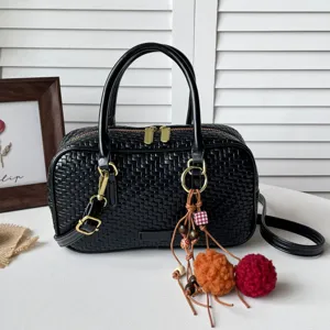 Schwarze geflochtene Boston-Tasche mit oberen Henkeln, goldener Hardware und süßen Anhängern.
