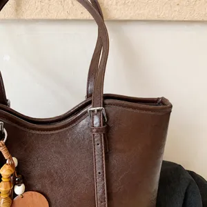 Vista detallada del bolso tote de cuero marrón con correa ajustable y abalorio de madera.