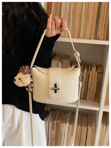 Chic niche design commuter bucket bag in litchi grain leather, shown with cute bear pendant detail.