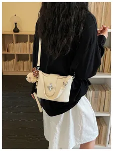 Detail view of a chic beige litchi pattern bucket bag with metal lock and cute bear charm pendant.
