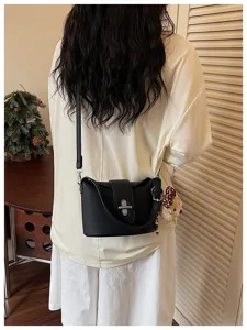 Detailed view of women black bucket bag with textured leather and cute bear charm pendant.
