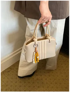 Close-up of beige canvas handbag with top handles, vertical stripes and beaded charm detail.