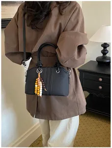 Detailed view of a stylish black dome handbag featuring wooden bead charms and strap.