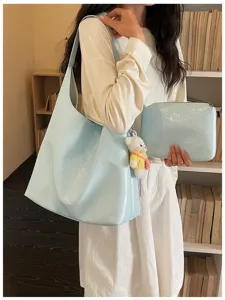 Detail view of a stylish light blue soft leather tote bag with matching clutch and bear charm.